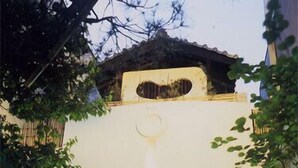 Un edificio con fachada de piedra, puerta de madera y un pequeño jardín con plantas.