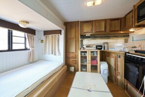 A compact RV kitchen with wooden cabinets, a stove, a microwave, and a small dining table.