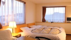 Quarto de hotel com cama, escrivaninha, cadeira e duas janelas com cortinas.