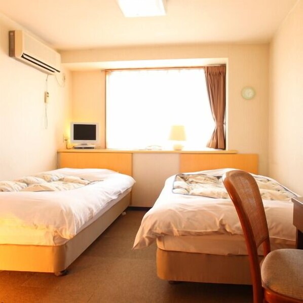 Una habitación de hotel con dos camas individuales, un escritorio con computadora, una ventana con cortinas y un equipo de aire acondicionado.