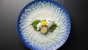 A blue plate with a decorative pattern, containing a white substance, garnished with green leaves, a yellow flower, and a slice of lime.