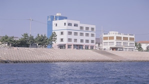 A coastal building with a flat roof, a visible water body in the foreground, and a clear sky.