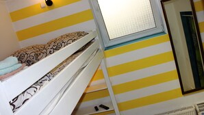 Una cama tipo litera con almohadas estampadas, una lámpara fijada a la pared y un espejo.