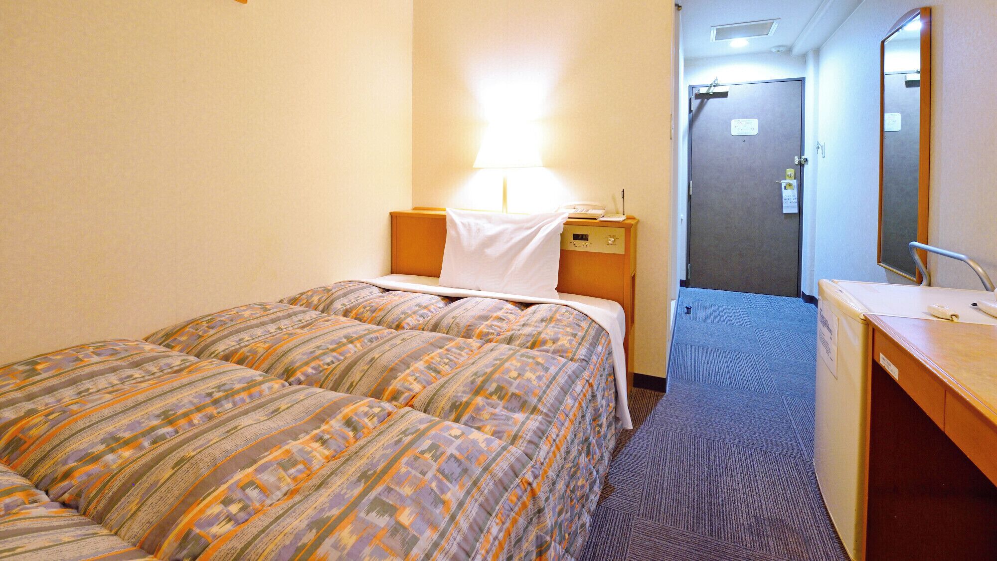 Hotellihuone, jossa on kaksi sänkyä, kirjoituspöytä peilillä ja ovi, joka johtaa kylpyhuoneeseen.