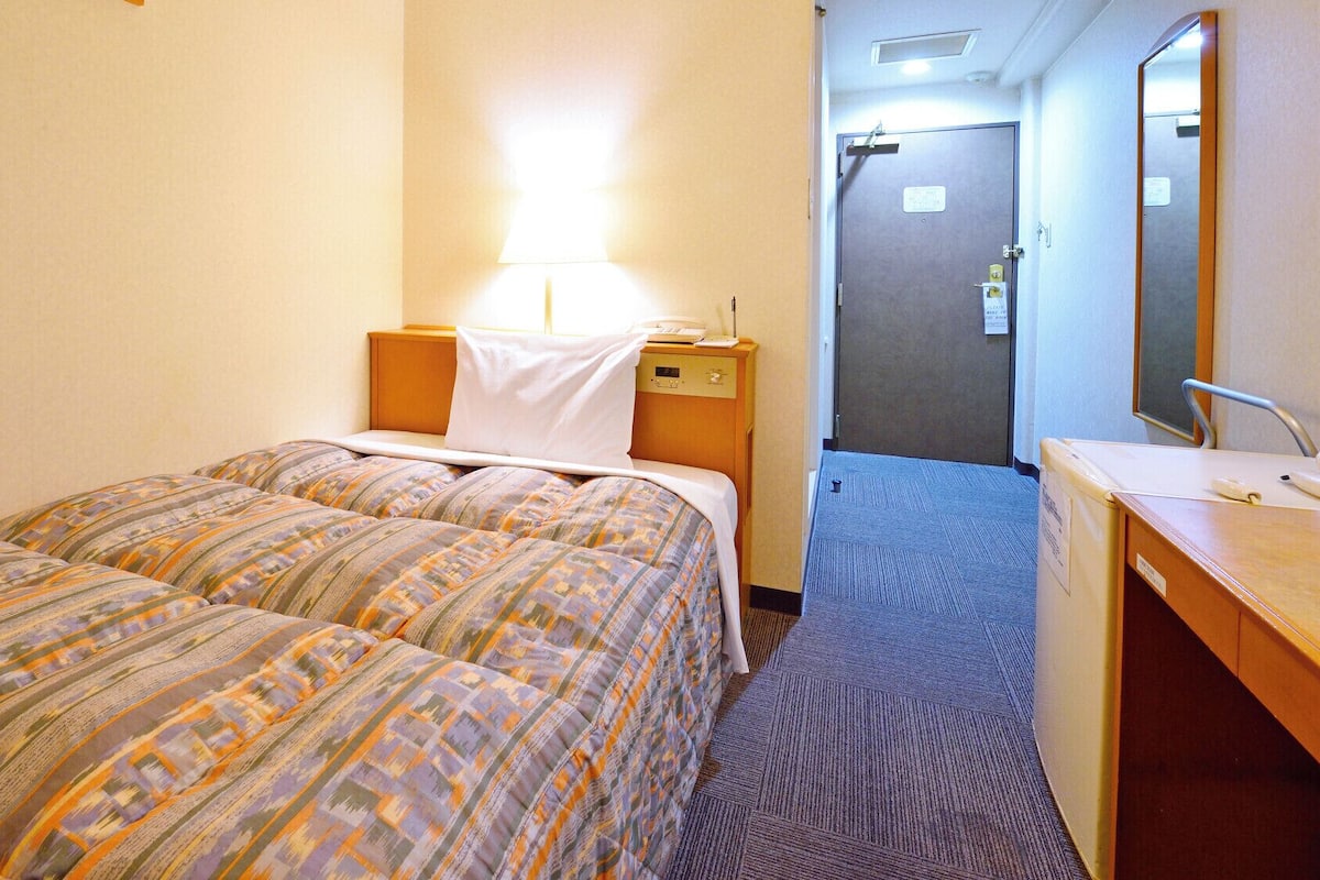 A hotel room with two beds, a desk with a mirror, and a door leading to a bathroom.