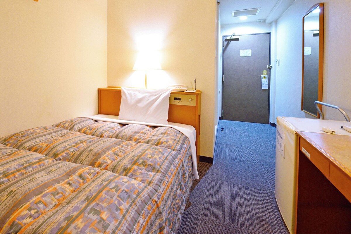 A hotel room with two beds, a desk with a mirror, and a door leading to a bathroom.