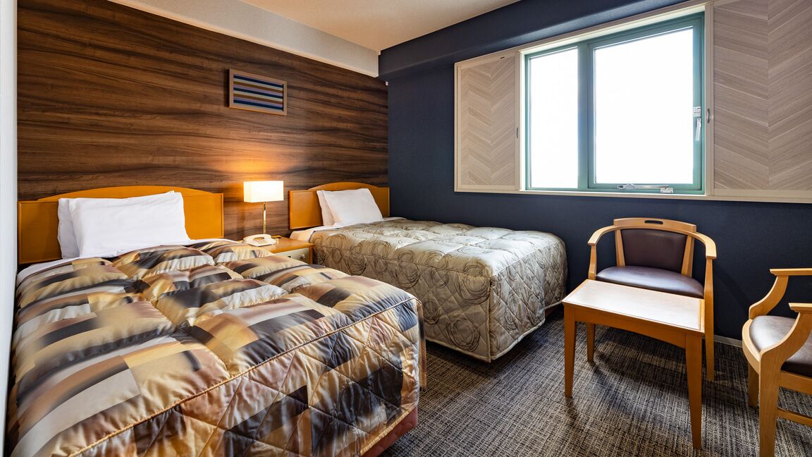 Hotellihuone, jossa on kaksi sänkyä, työpöytä ja tuoli.