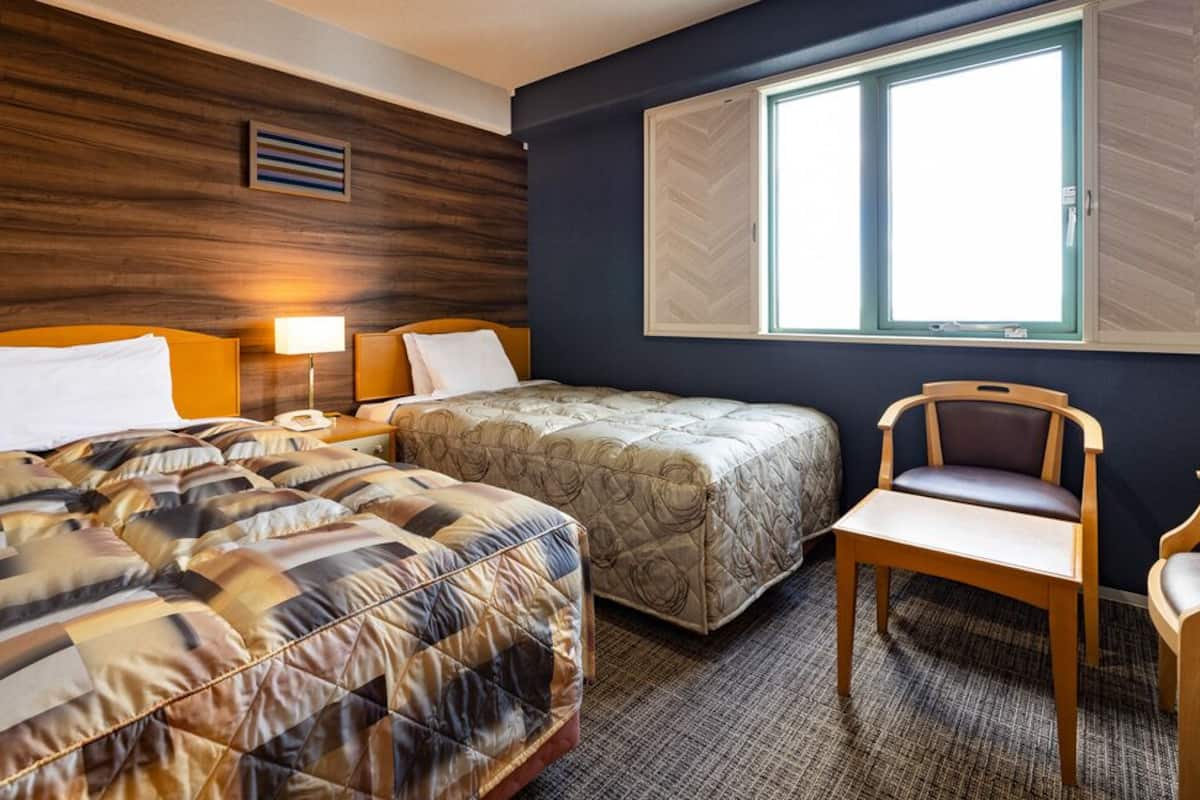 A hotel room with two beds, a desk, and a chair.