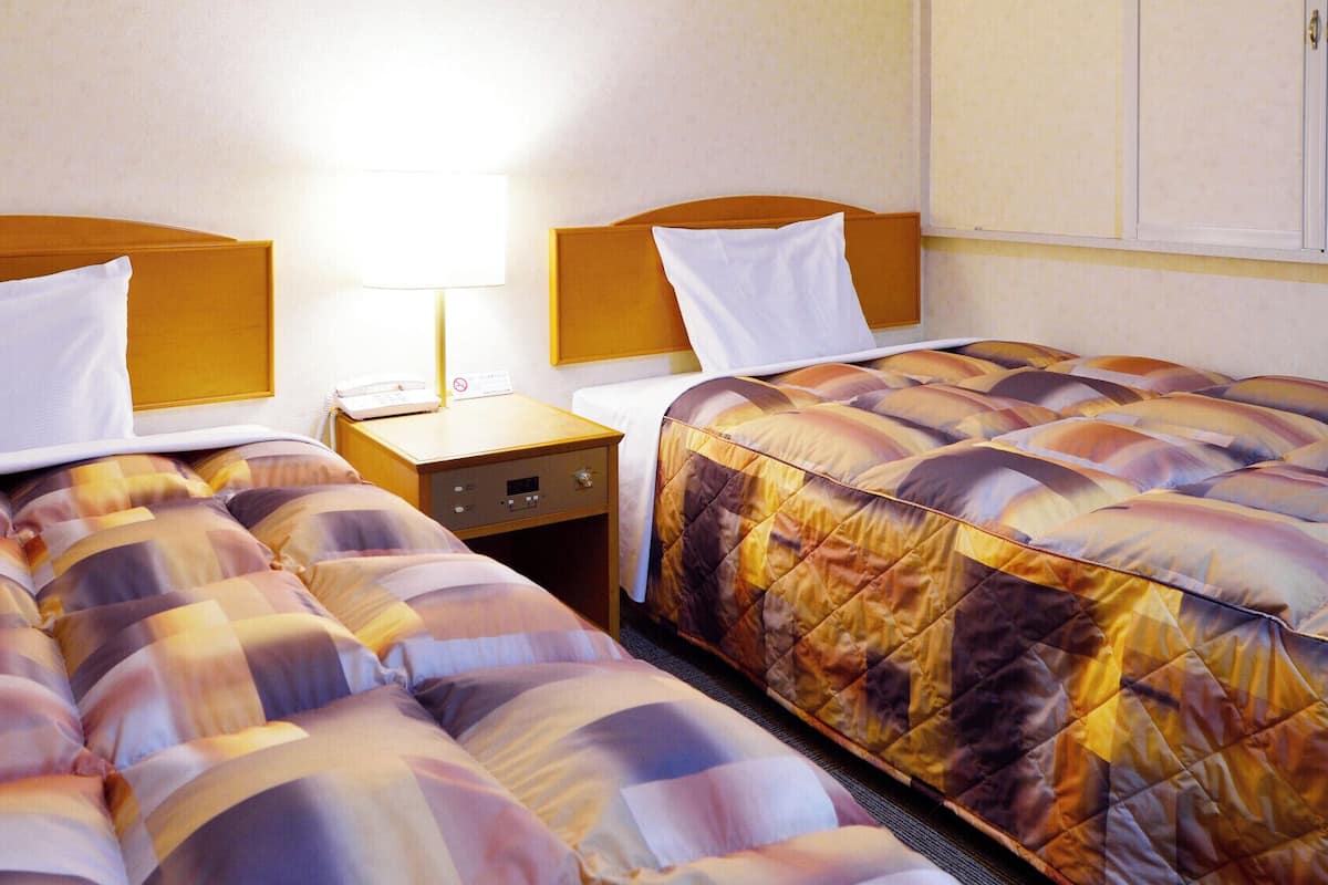 A hotel room with two beds, a nightstand with a lamp, and a wall-mounted cabinet.