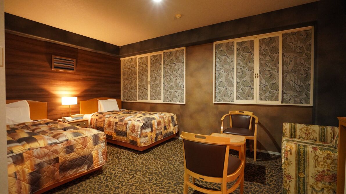 Hotellihuone, jossa on kaksi sänkyä, tuoli, työpöytä ja koristeelliset seinäpaneelit.