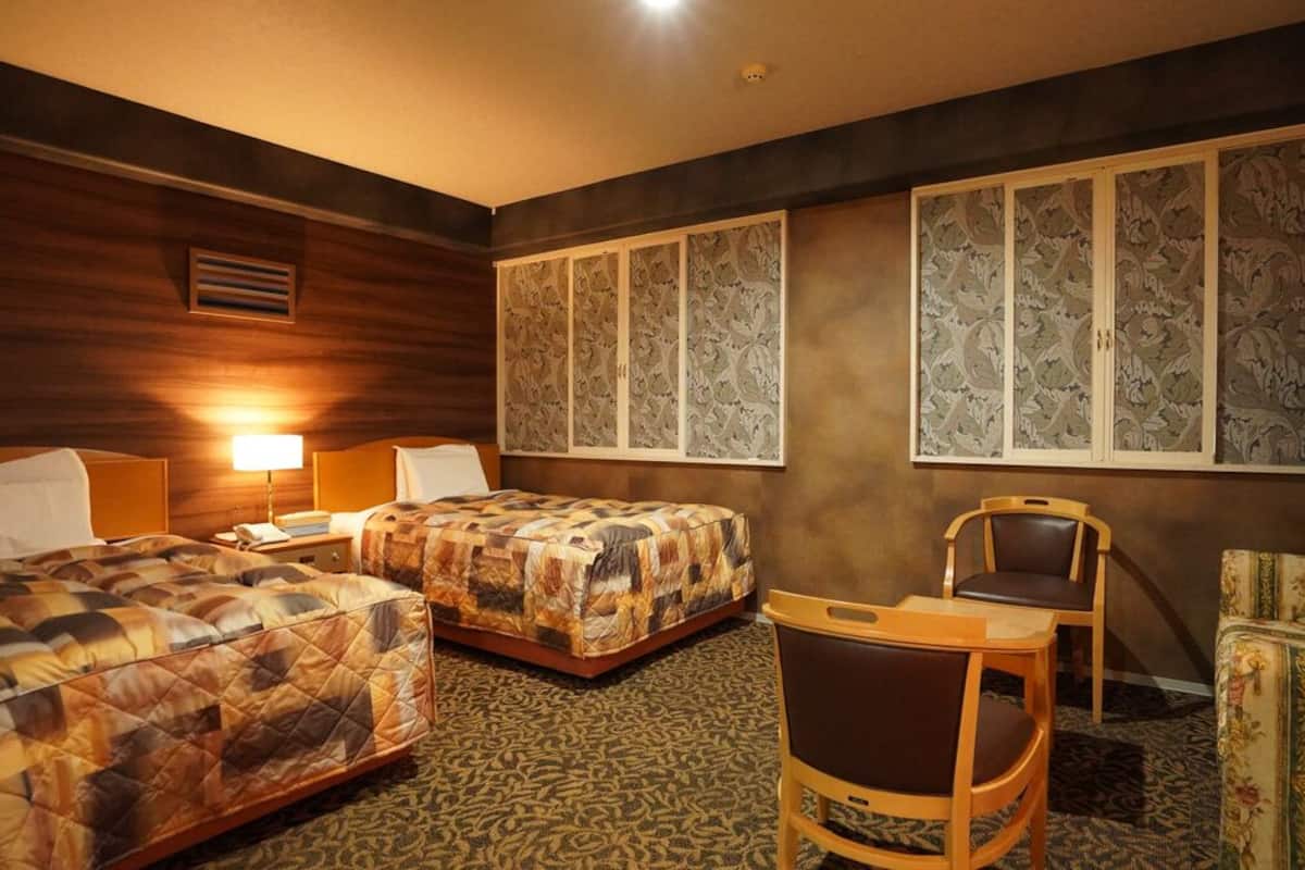 A hotel room with two beds, a chair, a desk, and decorative panels on the walls.