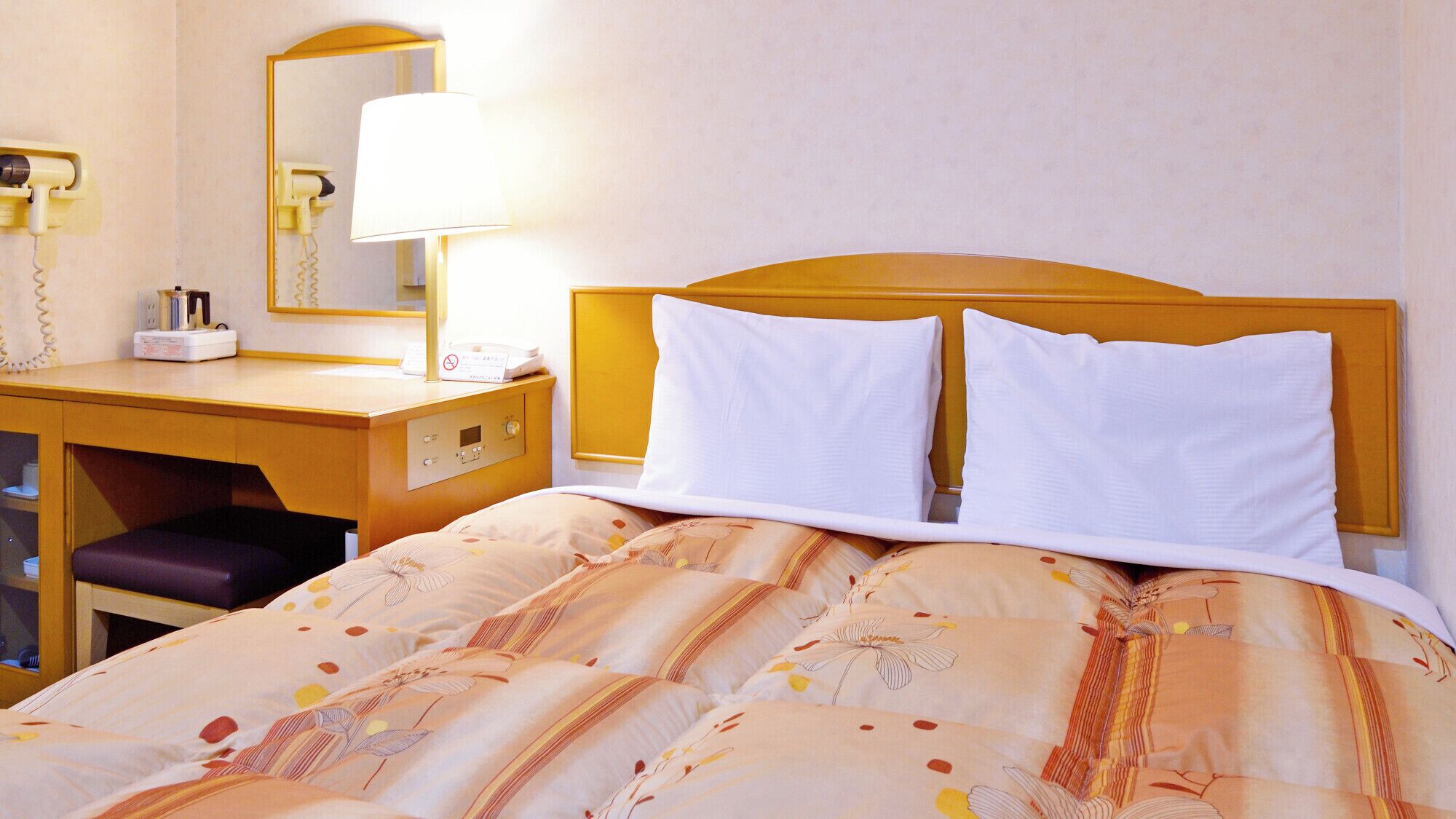 Hotellihuone, jossa on sänky, kirjoituspöytä, jossa on puhelin, ja peili.
