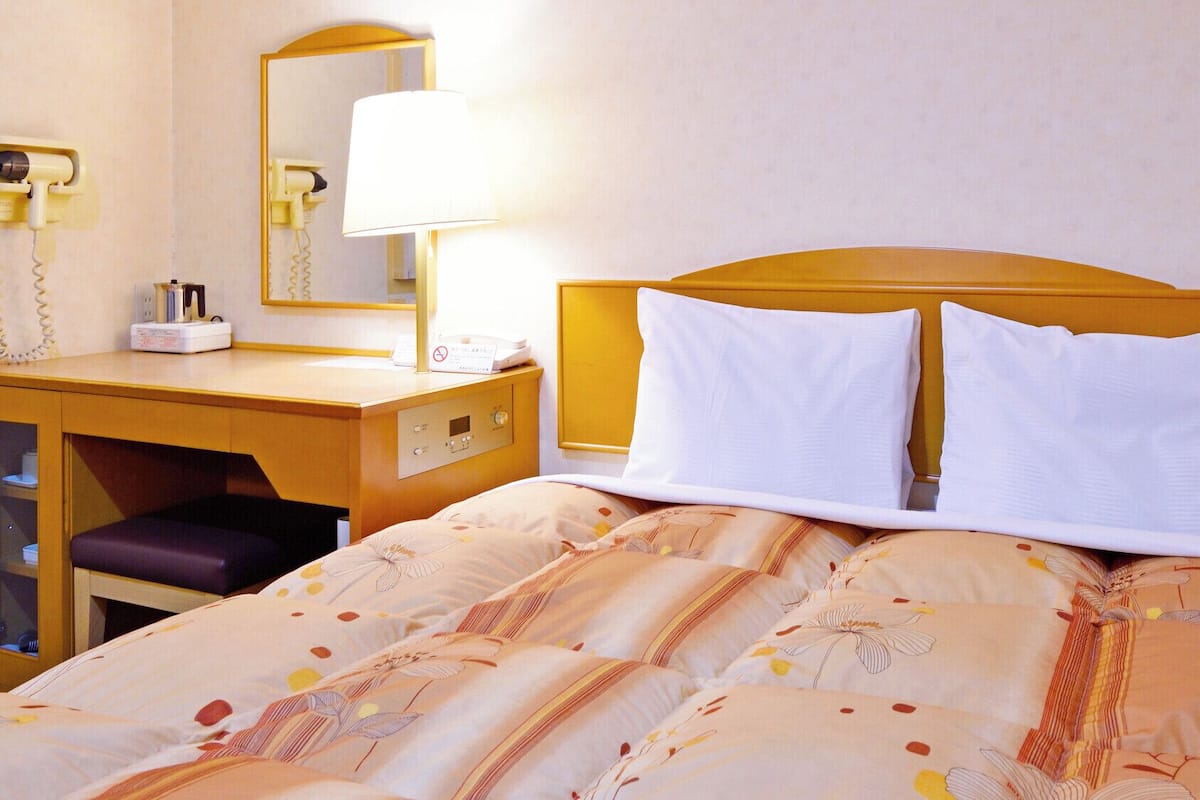 A hotel room with a bed, a desk with a telephone, and a mirror.