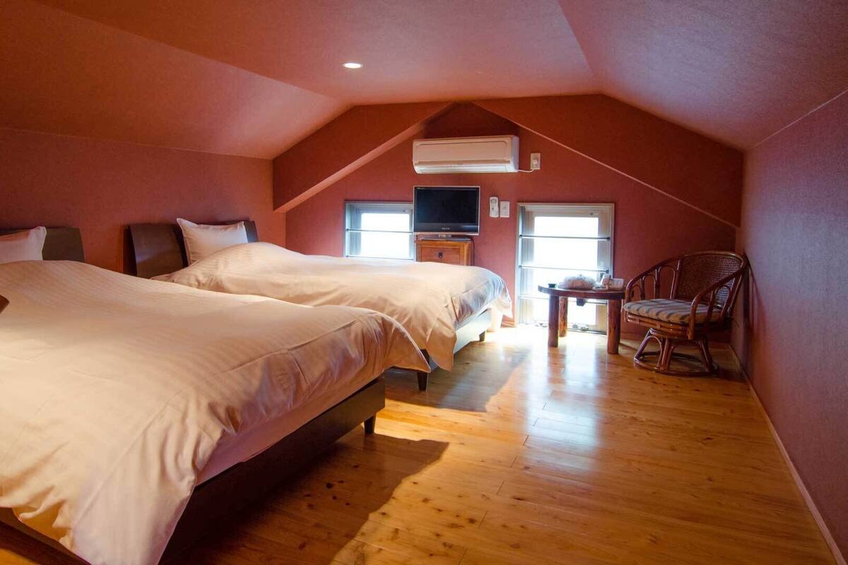 A bedroom with two beds, a TV, a chair, and a window.