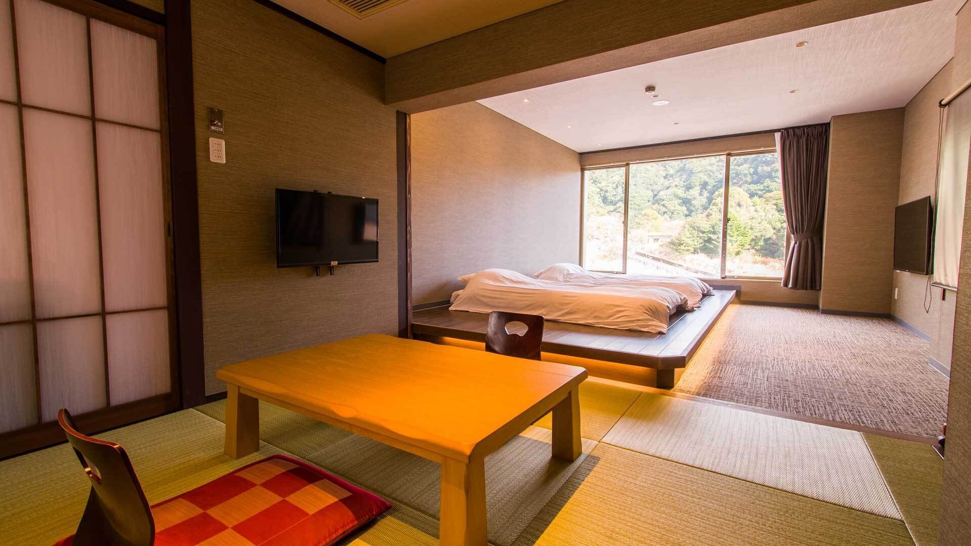 A room with tatami flooring, a low table, a bed with a view, and a TV.