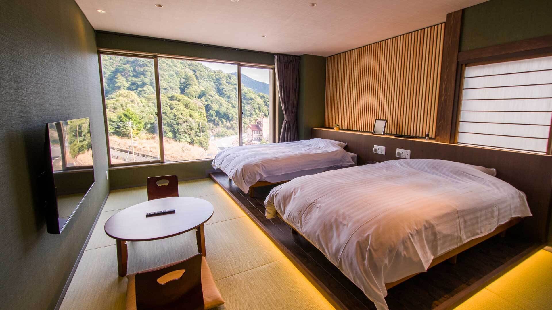 Habitación de hotel con dos camas, televisor, una mesita y vista a un bosque.