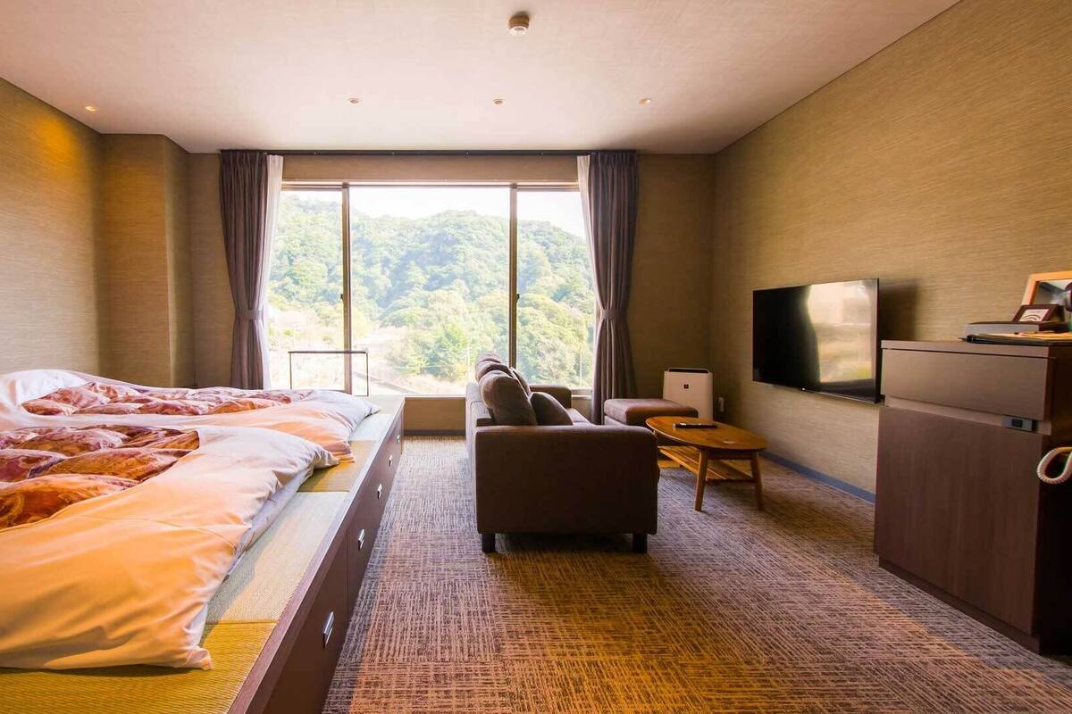 A hotel room with a large bed, a sofa, a TV, and a view of the outdoors.