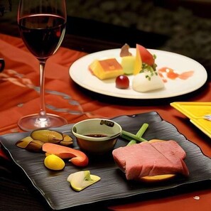 A dining table with a plate of food, a glass of red wine, and a bowl of sauce. - Kirishima Onsen Oyado Hana Mizuki (Kirishima)