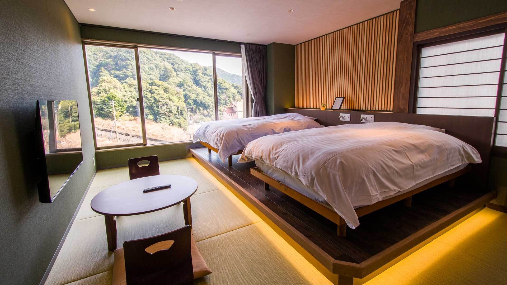 Un dormitorio con dos camas, televisión, una mesa y vista a un bosque.