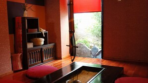 A room with a wooden floor, a small table with a sand tray, red cushions, a shelf with baskets, and a window with a red blind. - Kirishima Onsen Oyado Hana Mizuki (Kirishima)
