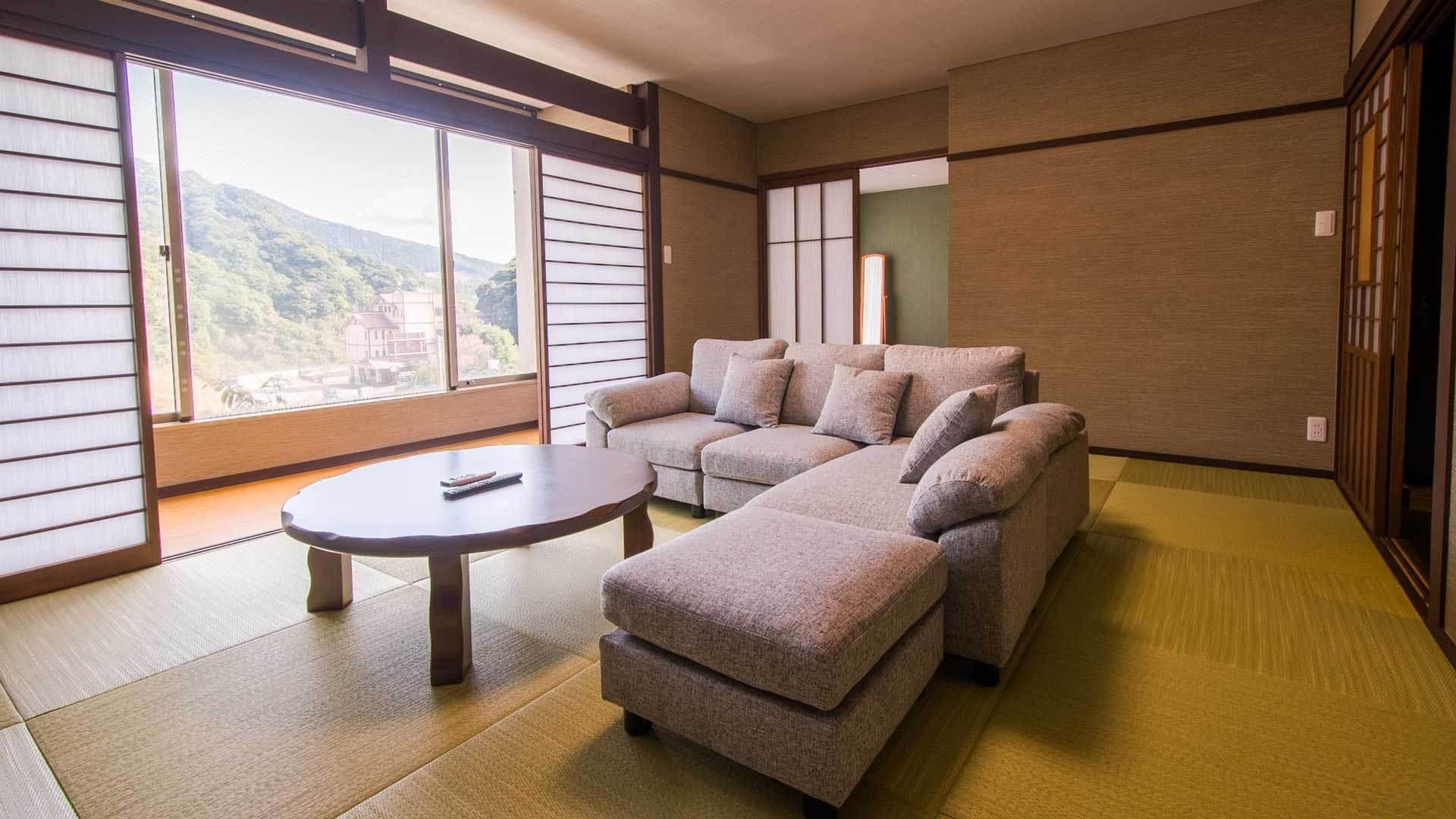 Una habitación con suelo de tatami, un conjunto de sofás, una pequeña mesa redonda y una puerta corredera con vistas a la montaña.