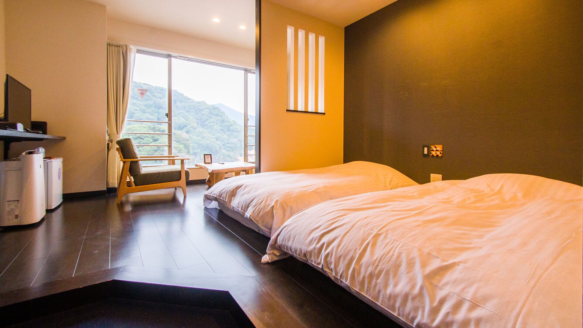 Habitación de hotel con dos camas, un escritorio, una silla y vista a un paisaje montañoso.