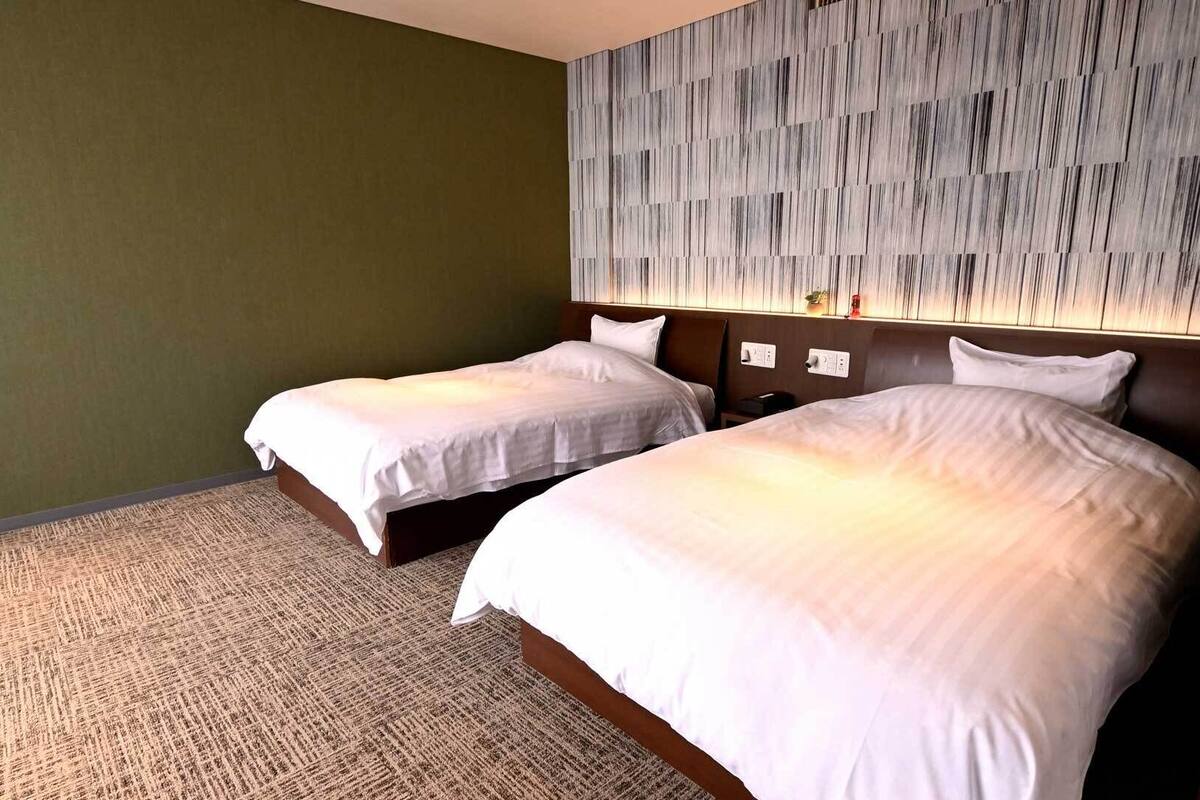 A hotel room with two beds, a patterned wall, and a carpeted floor.