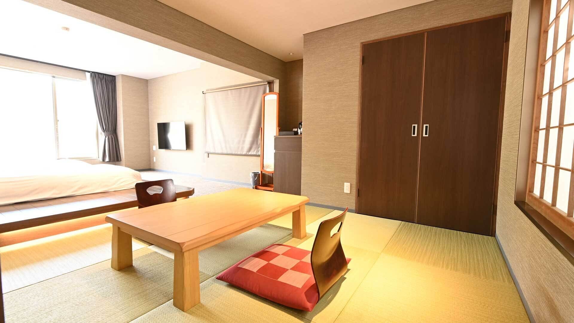 Una habitación de hotel con cama, una mesa de madera, una silla, televisor, armario y esteras de tatami.
