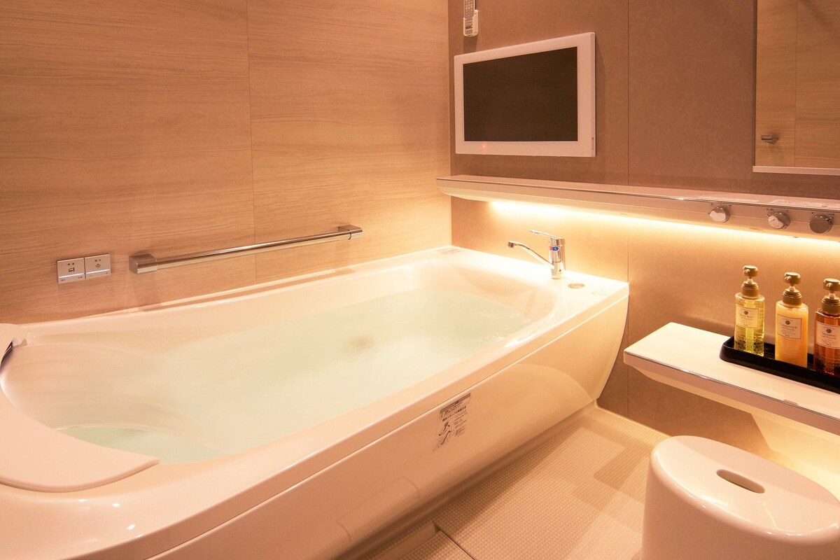A modern bathroom with a large bathtub, a toilet, and a shelf with toiletries.