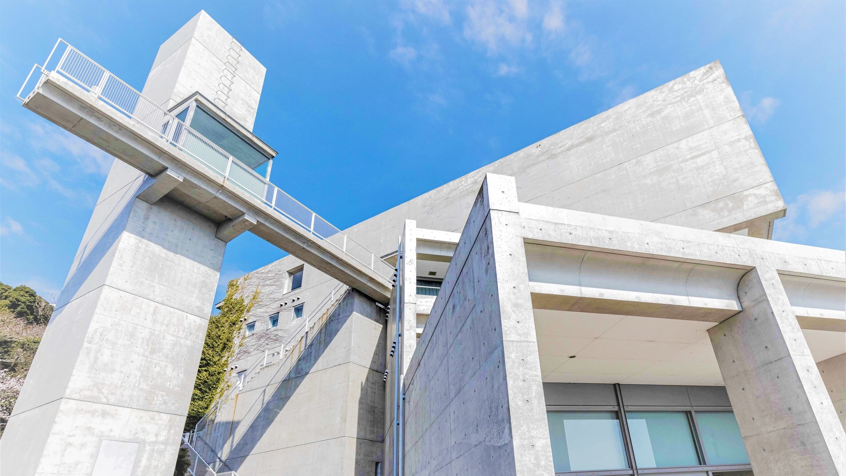 A modern building with a concrete facade, a pedestrian bridge, and a staircase leading to an upper level.