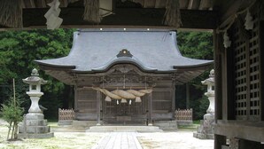 A traditional Japanese building with a curved roof, a central entrance, and two stone lanterns on either side. - Ryokan Asahikan (Yasugi)