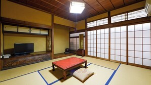 A traditional Japanese room with tatami flooring, a low wooden table, a television, and sliding shoji doors. - Ryokan Asahikan (Yasugi)