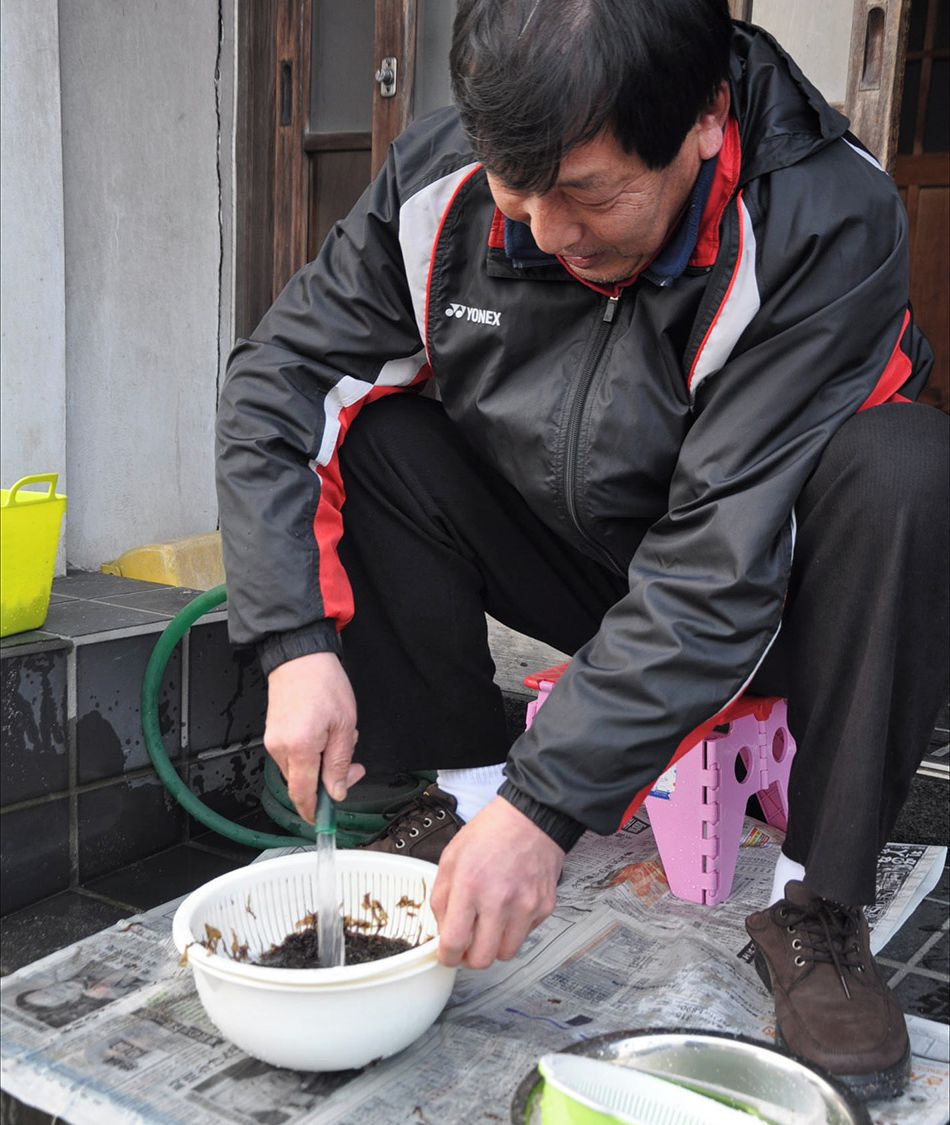 A person kneeling on a stool, scooping soil from a white bowl.