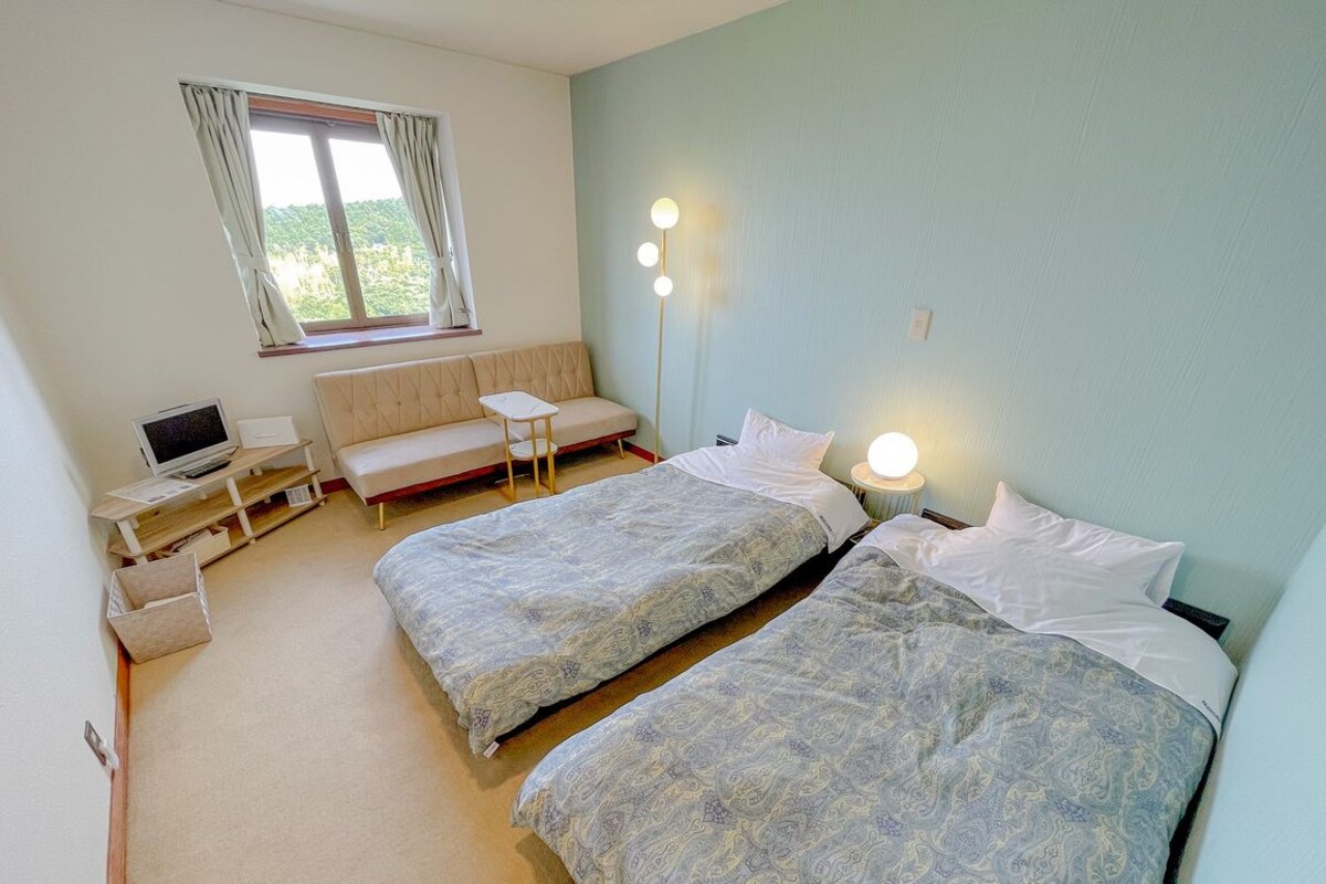 A bedroom with two beds, a desk, a chair, and a window with curtains.