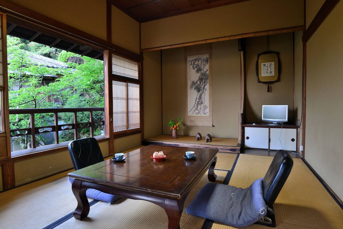 A traditional Japanese room with tatami flooring, a wooden table, and a television on a cabinet.