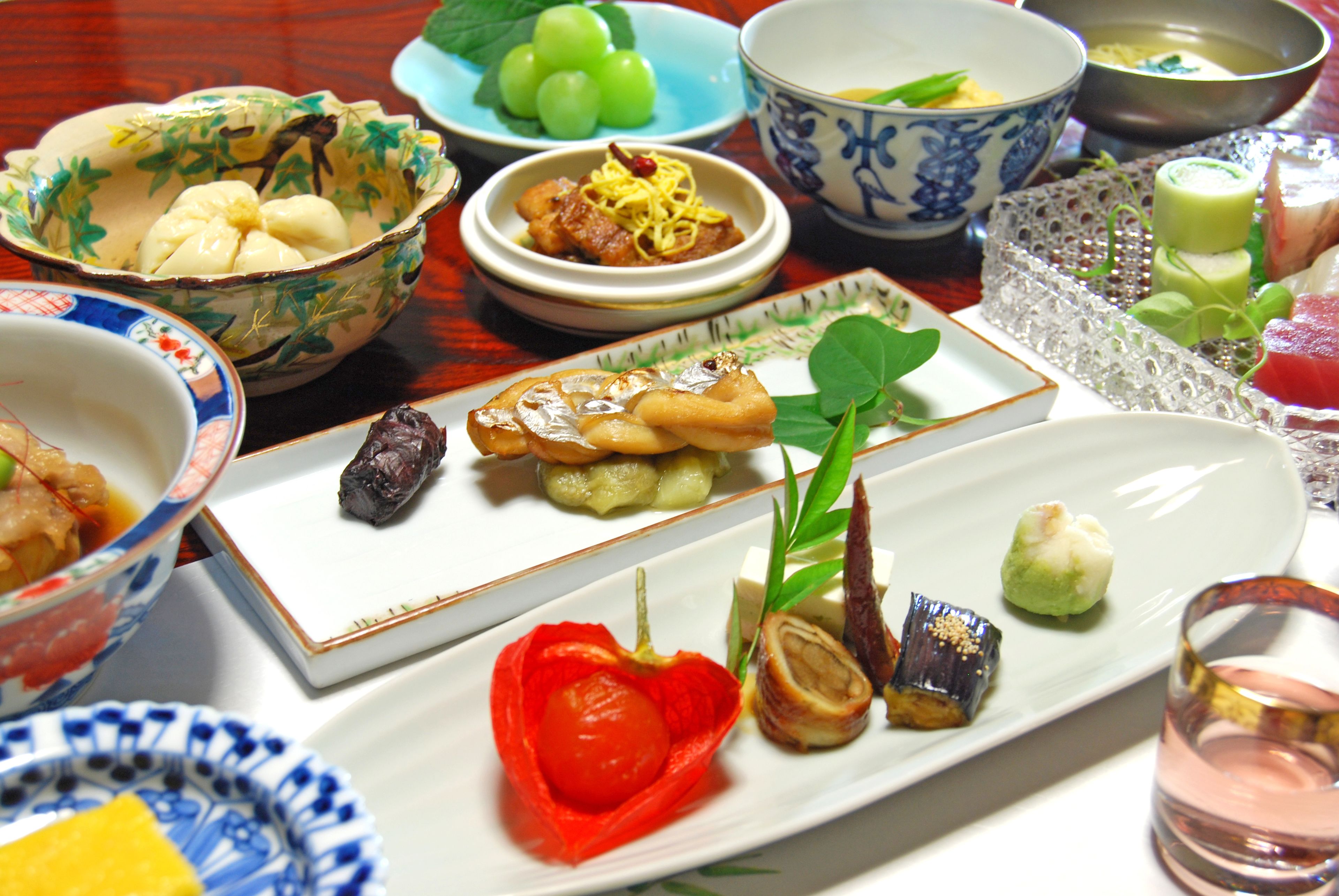 Une variété de plats sont disposés sur la table, notamment des sushis, des raviolis et un bol de raisins verts.