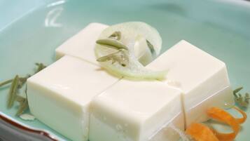 A dish with tofu cubes, a slice of cucumber, and some herbs.