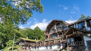 A traditional chalet with a wooden balcony, stone walls, and a thatched roof. - Hope Lodge (Chino)