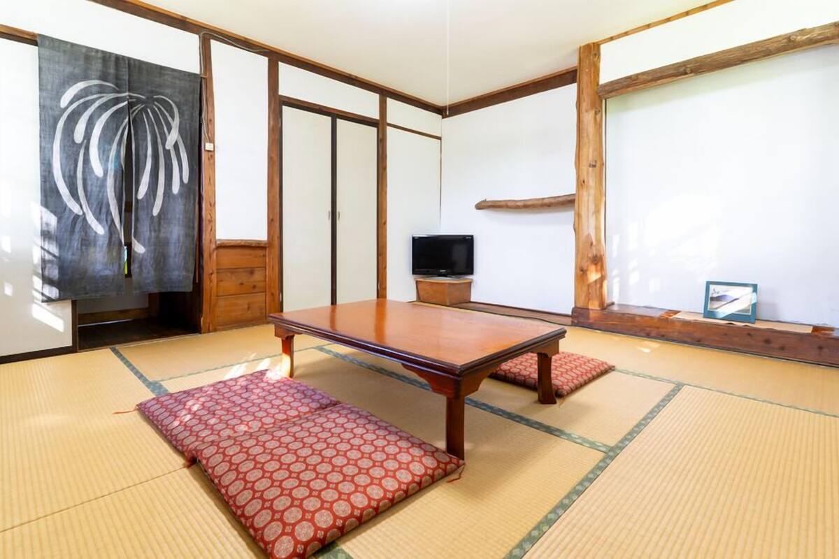A traditional Japanese room with tatami flooring, a wooden table, a television, and sliding doors.