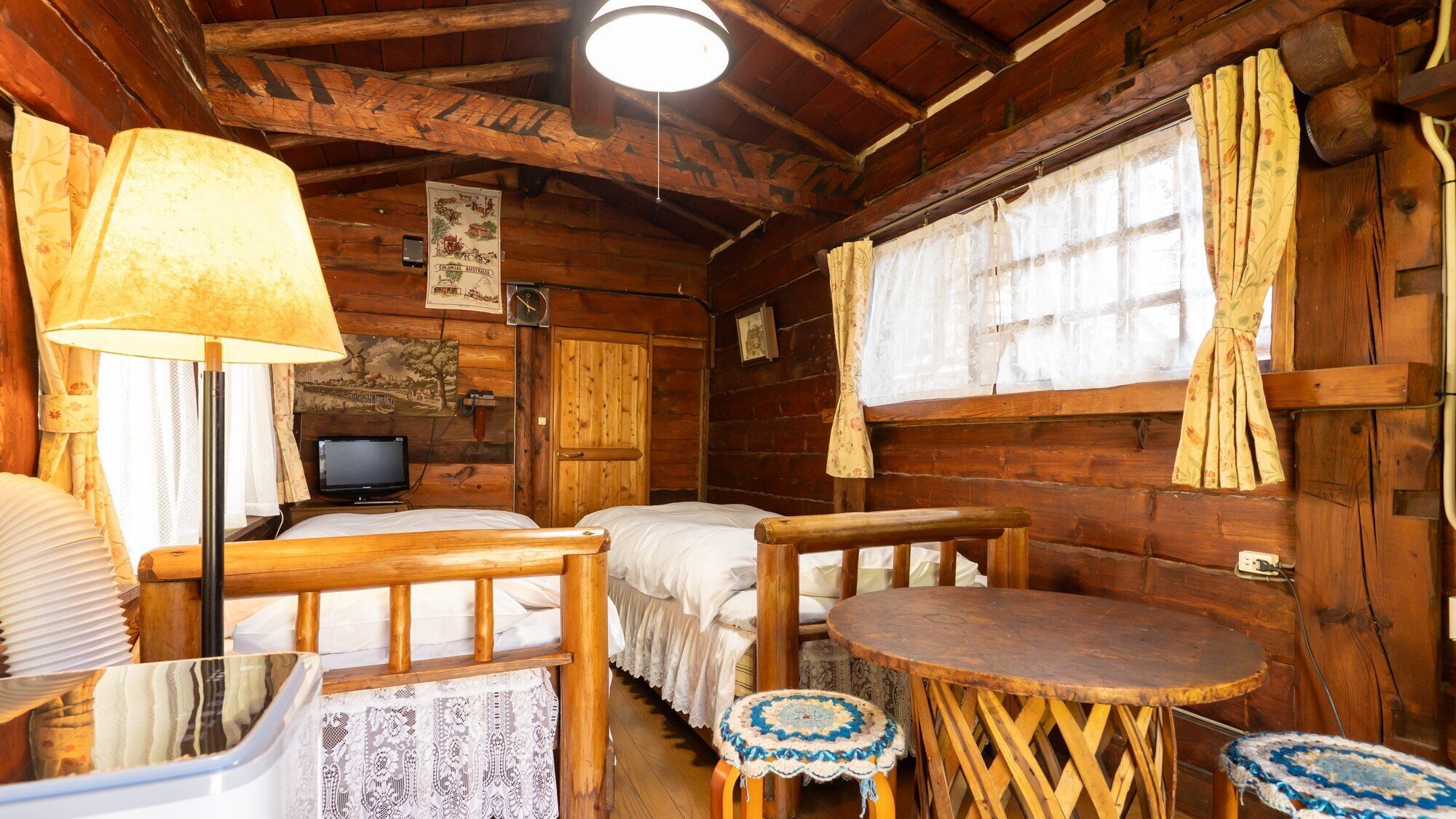 A rustic cabin with wooden walls, a bed, a table, a lamp, and a television.
