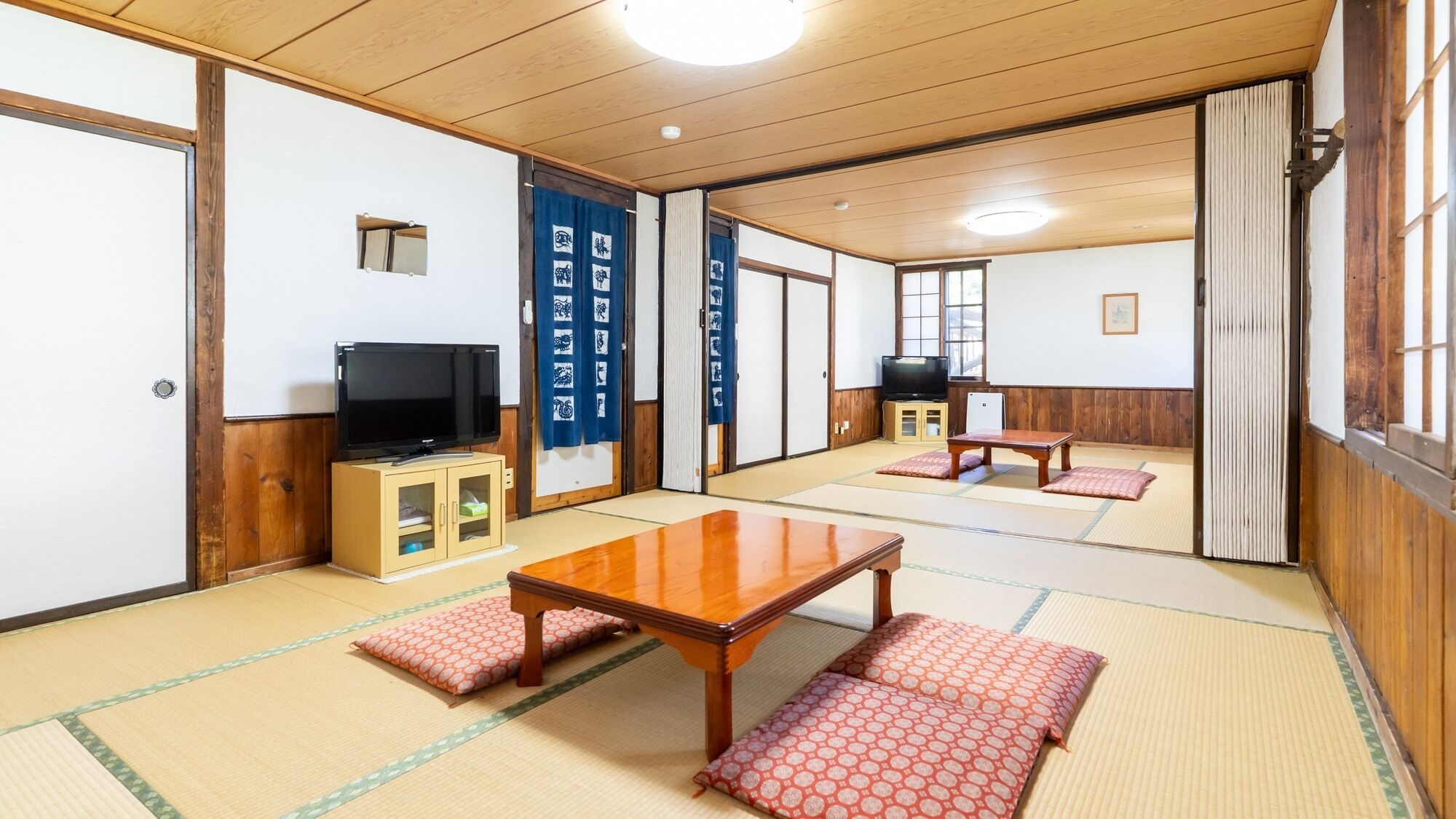 A traditional Japanese room with tatami flooring, a television, a table, and sliding doors.