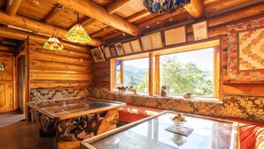 A rustic wooden cabin interior with a glass-top table, wooden benches, and a view of the outdoors through large windows. - Hope Lodge (Chino)