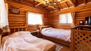 A log cabin room with two beds, a chandelier, a television, and a clock. - Hope Lodge (Chino)