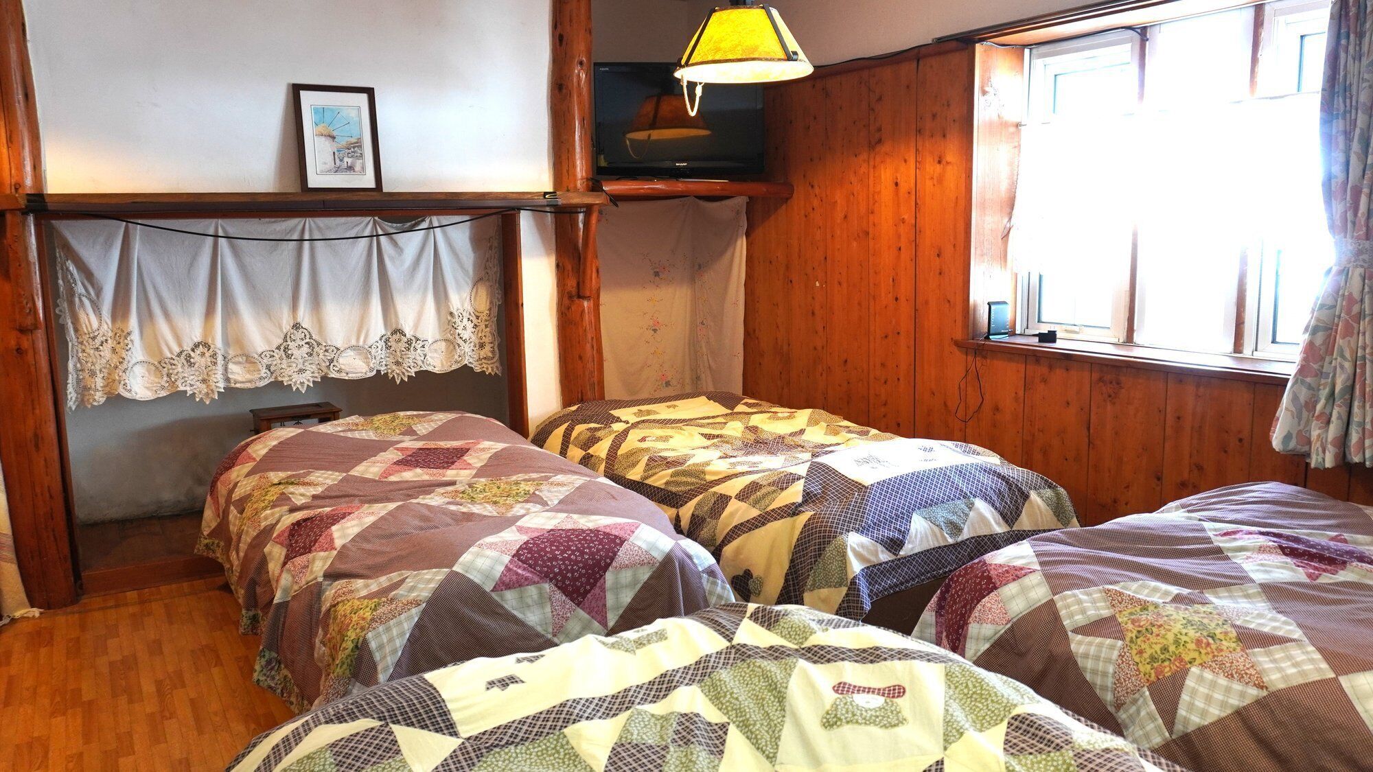 A room with four beds, a television, a lamp, and a window with curtains.