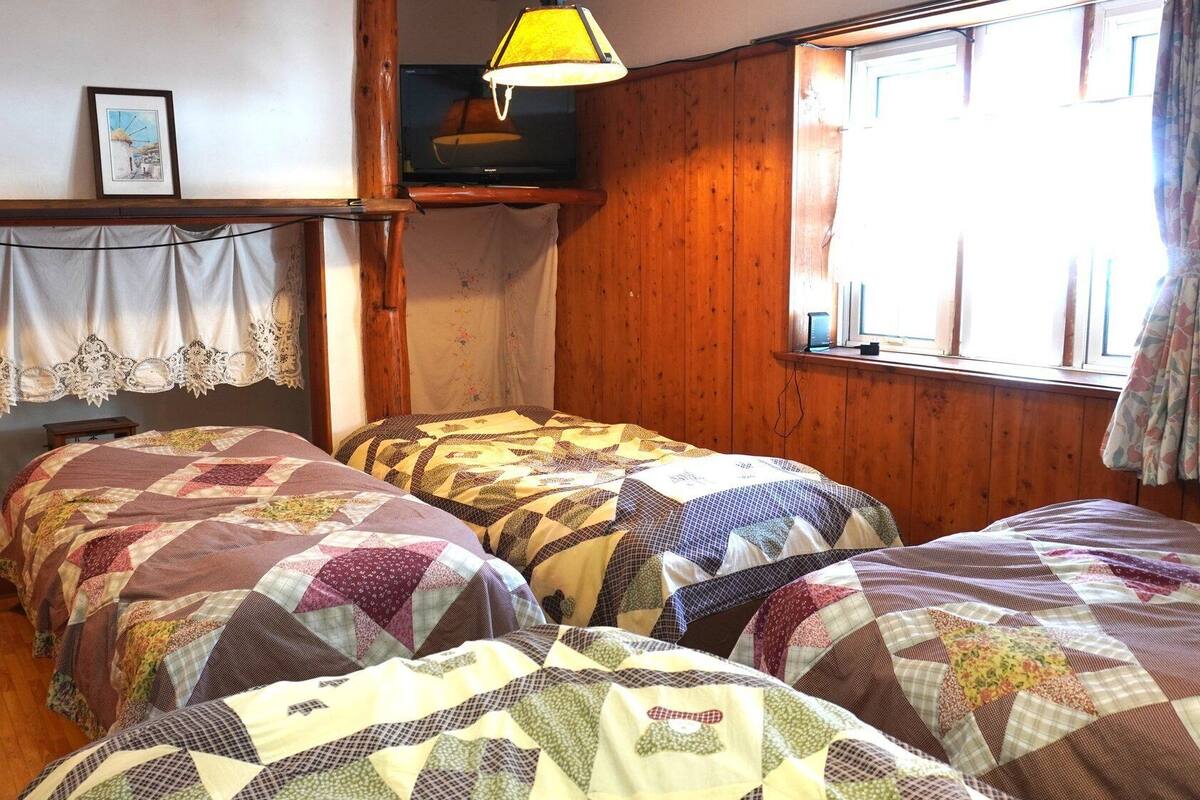 A room with four beds, a television, a lamp, and a window with curtains.