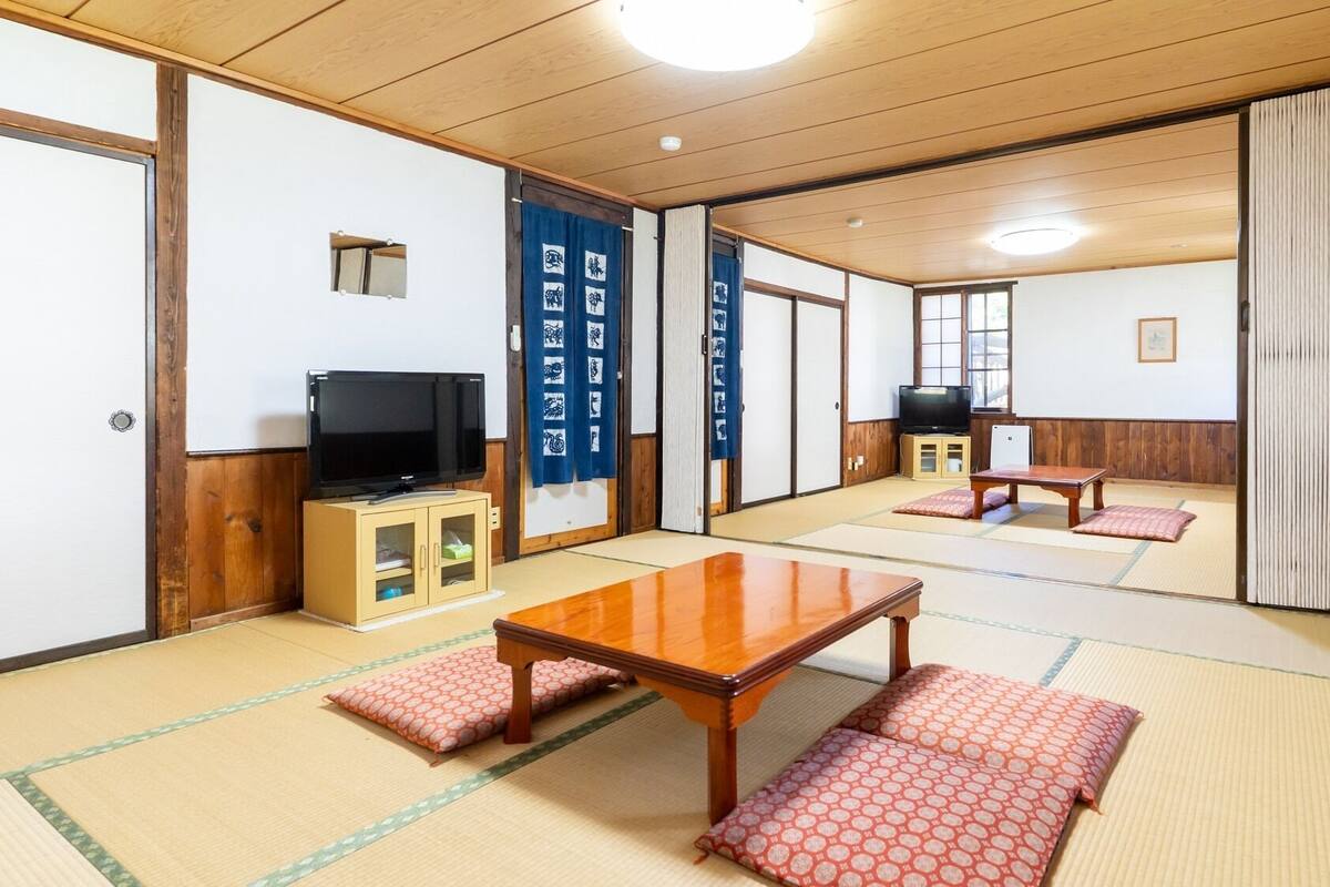 A traditional Japanese room with tatami flooring, a television, a table, and sliding doors.