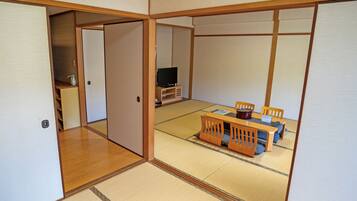 A traditional Japanese room with tatami flooring, a low table with chairs, and a television.