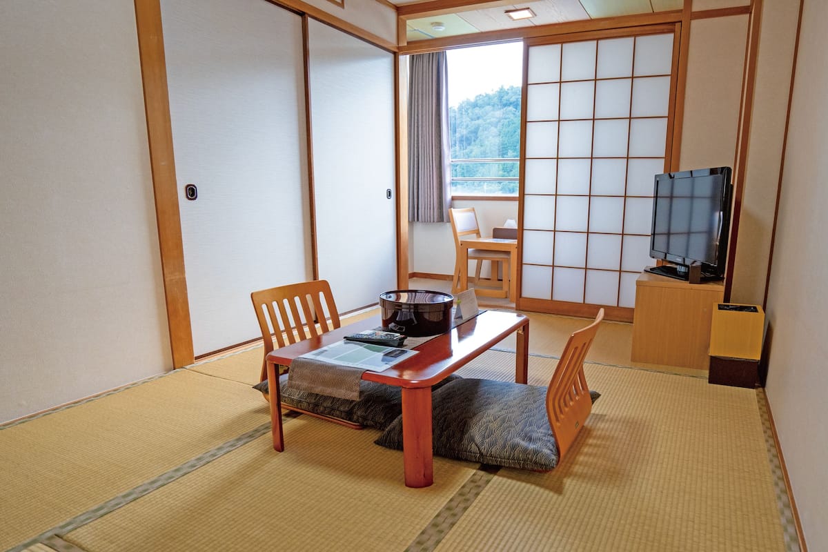 A traditional Japanese room with tatami flooring, a low table with cushions, a television, and sliding doors.