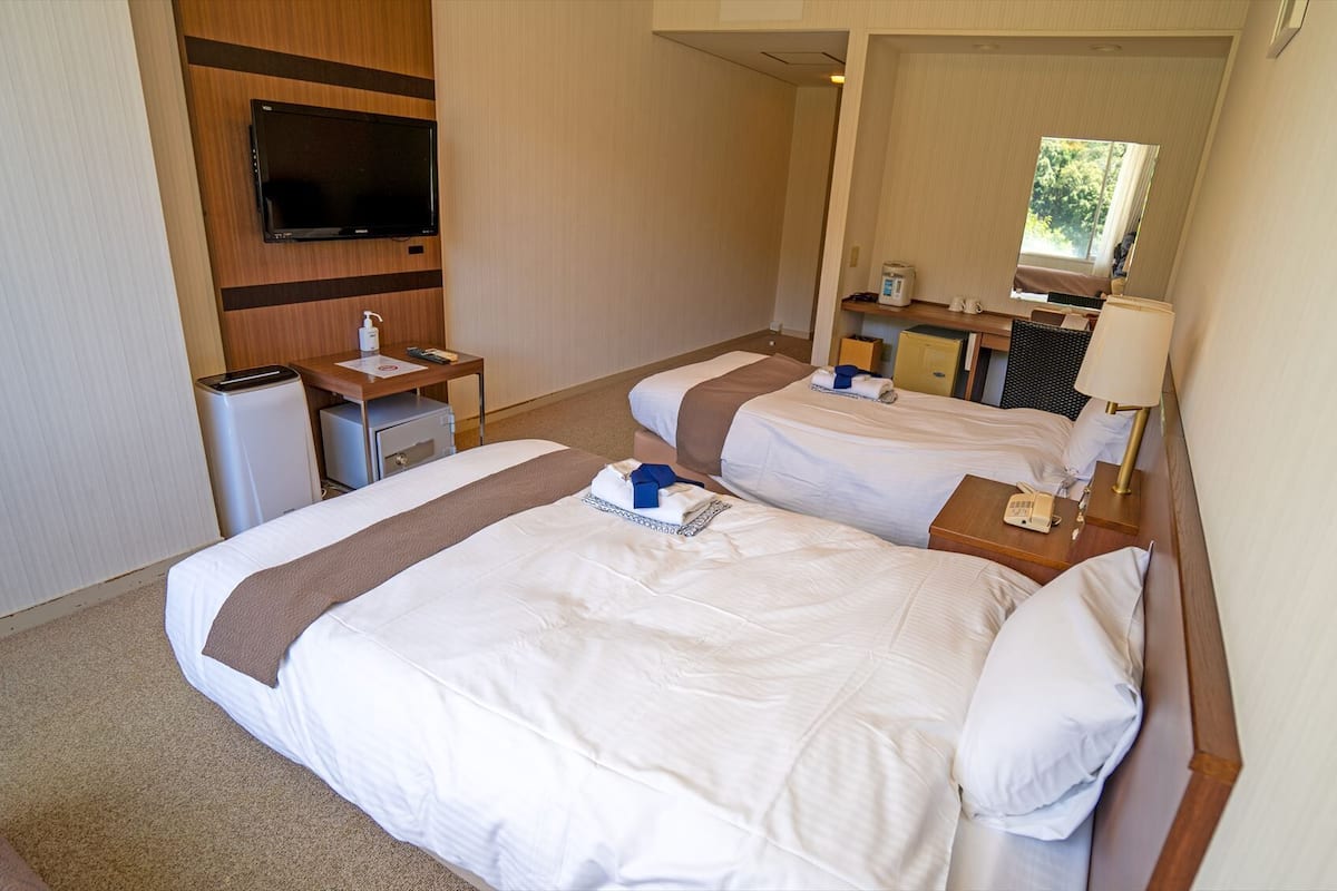 A hotel room with two beds, a TV, a desk, and a mirror.