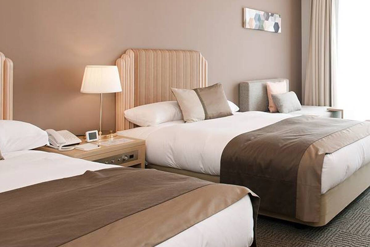 Quarto de hotel com duas camas, mesa de cabeceira com abajur, telefone e uma tela pequena.